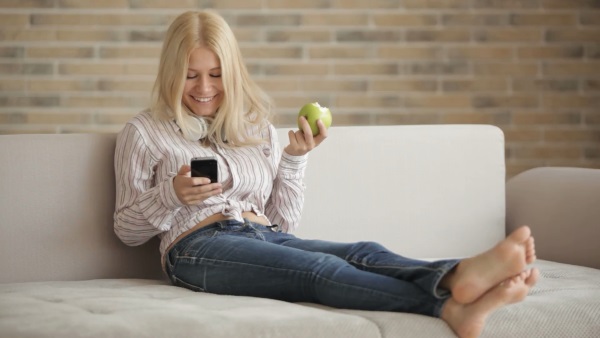 жінка на дивані з телефоном і яблуком